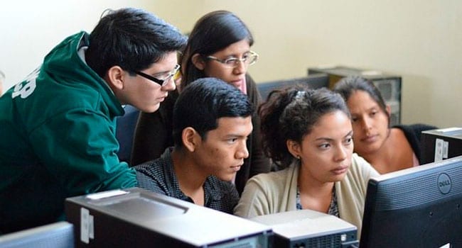 Students looking over shoulder of another student sitting at a computer