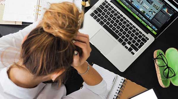 Stressed woman holding her head, staring down at her desk